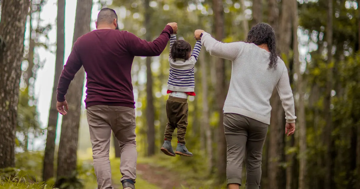 Two parents walking through a forest with a small child between them