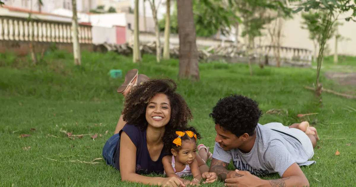 A family lying on the grass in a park, a baby between the two parents